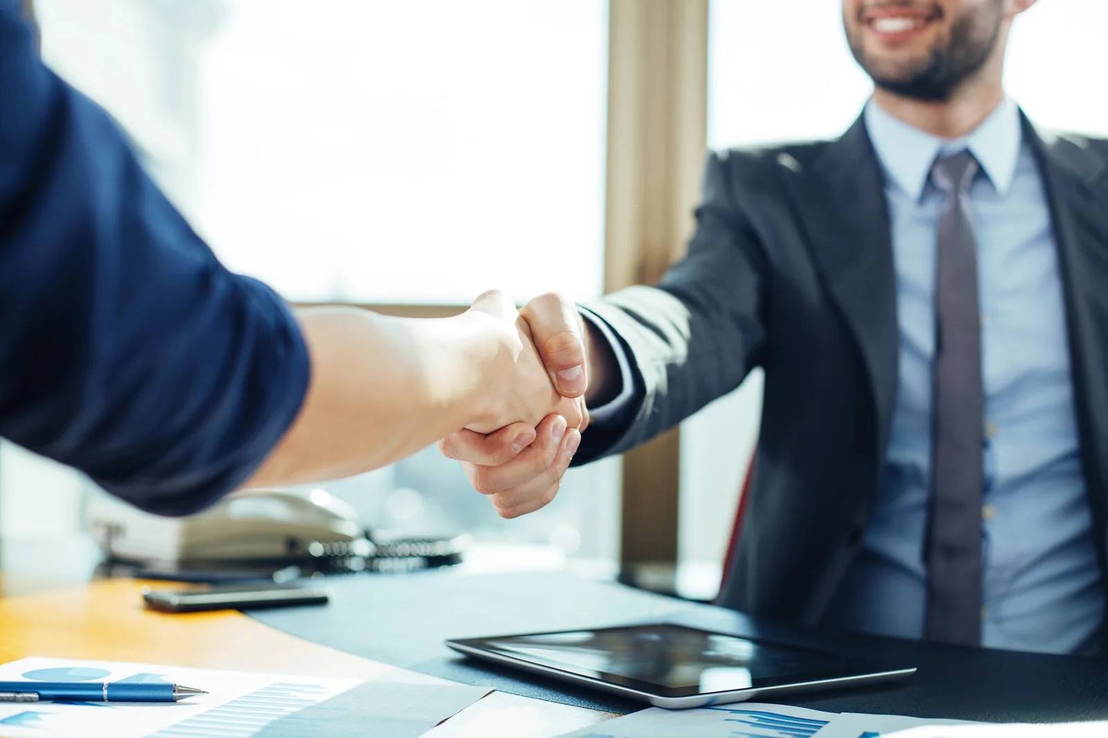 Two people shaking hands across a desk in an office